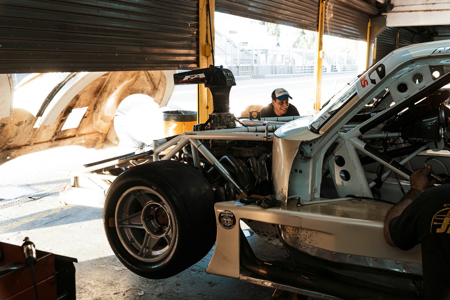 Monteurs die aan een raceauto werken in een garage met een racecircuit buiten.