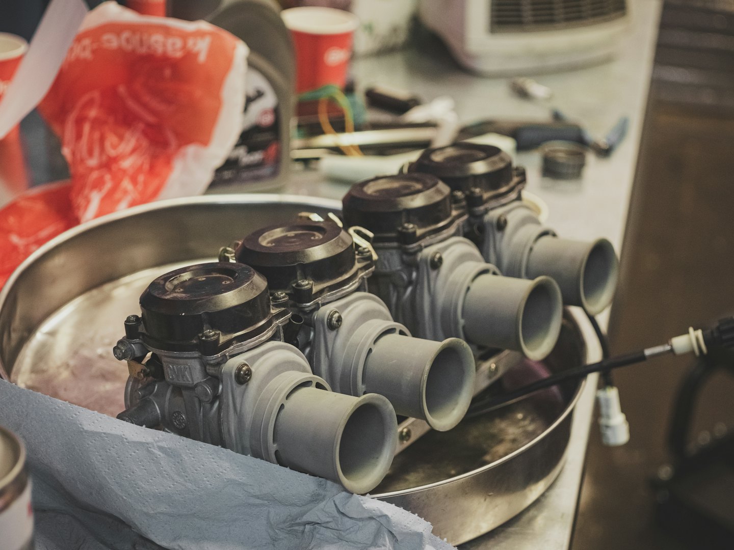 Vier carburateurs van motorfietsen in een metalen bak op een werkbank.