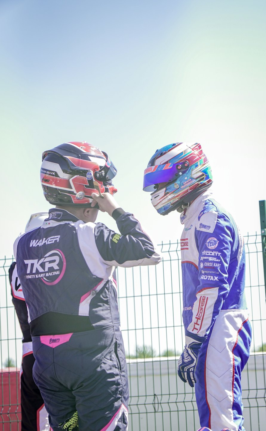 Twee autocoureurs staan samen bij een hek langs het circuit.